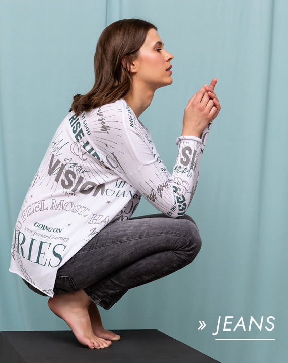 Model trägt weißes Langarmshirt und Jeans hockend