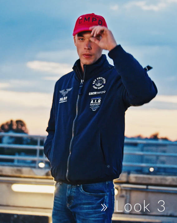 Model trägt rotes Base Cap und dunkelblaue Jacke