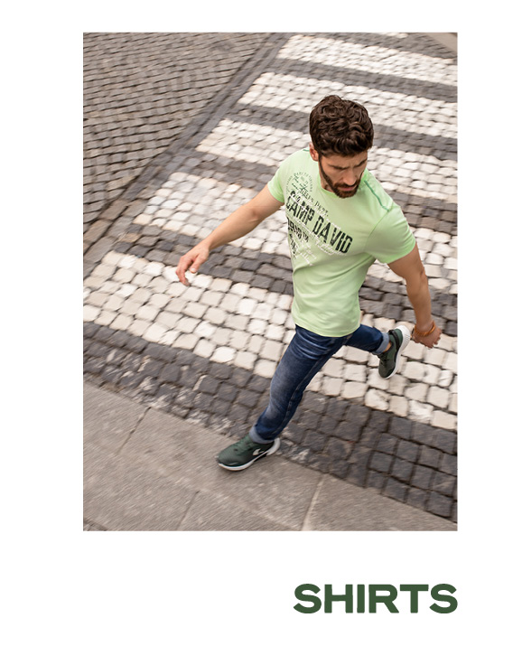 Model trägt ein grünes Artworkshirt und läuft über die Straße.